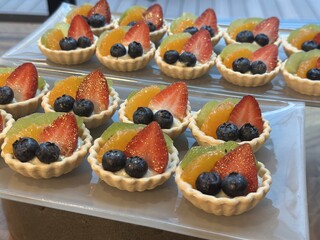 Mini fruit tarts arranged on trays with fresh berries and citrus topping creamy pastry for festive dessert catering