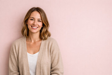 Obraz premium Horizontal portrait photo of a smiling woman in a beige cardigan on a soft pink background, expressing gentle optimism, emotional comfort, relaxed mindset for mental wellbeing/positive states of mind