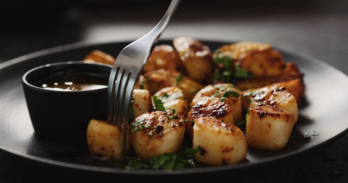 eat roasted scallops with baked potatoes on black plate