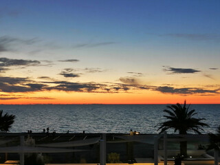 Seashore, silhouettes of people, palm trees, sunset, the sun setting over the horizon