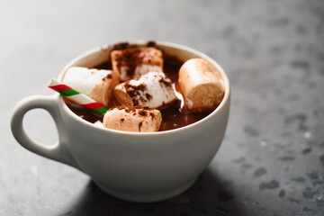 Cocoa drink with marshmallow and christmas drinking straw in white cup on terrazzo surface with copy space