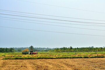 Fototapeta premium Wide view of farmland after harvest with straw bales, power lines, and farming equipment in a rural countryside setting in Theni, Tamilnadu 