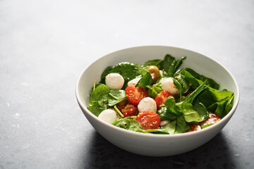 Salad with cherry tomatoes, spinach leaves and mozzarella balls in white bowl on terrazzo surface with copy space