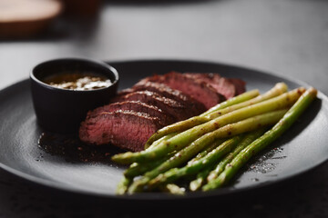 New york steak with asparagus on black plate with pesto sauce