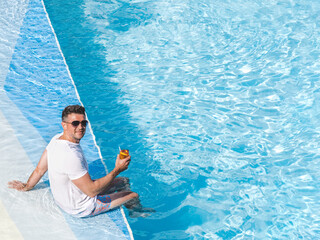 Handsome man relaxing with a drink by the cruise ship pool on a sunny, clear morning. Top view. Vacation and travel concept. Chill lifestyle, luxury travel. Perfect for holiday and travel themes