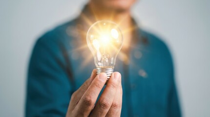 A person in a blue shirt holds a bright light source in their hand against a neutral background in a soft focus image