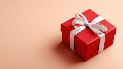Fototapeta premium A vibrant red box with a white ribbon and bow, casting a shadow on a light peach-colored surface. The box is centered