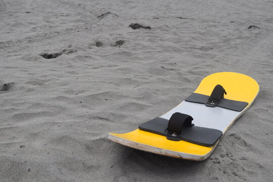 A yellow and silver sandboard lies on a vast expanse of gray sand