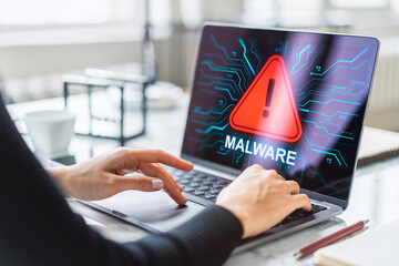 Woman using laptop with malware alert warning on screen at modern office desk showing cyber threat concept and digital data security breach.