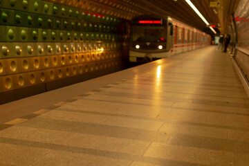 white passenger awaiting train on platform, empty station scene with approaching carriage and warm tunnel lights, tiled flooring and signage create depth, solitary figure near far edge