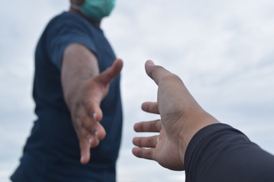 Two hands reaching out to help each other under a cloudy sky. A symbol of support and hope
