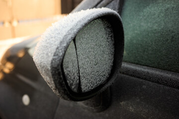 Frost covers a car side mirror during winter morning at an urban location in the early hours