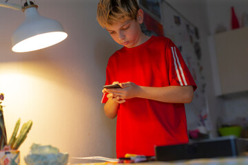 white boy checking smartphone under lamp light, red shirt, closeup of hands scrolling notifications, candid evening moment capturing digital habit and teen leisure, subtle warm glow