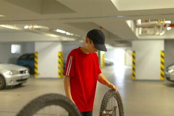 Man inspecting tire, Young male checking tire tread, Individual examining tire in parking garage setting, Young man in red shirt inspecting vehicle tire in industrial environment