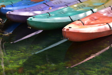 A brightly colored canoe floats on the water,A number of brightly colored kayaks float in the still water