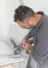 Obraz premium Craftman in grey shirt cuts a gray marble tile using an angle grinder. Handy men at work, hands closeup