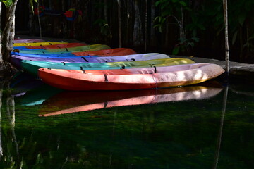 A brightly colored canoe floats on the water,A number of brightly colored kayaks float in the still water