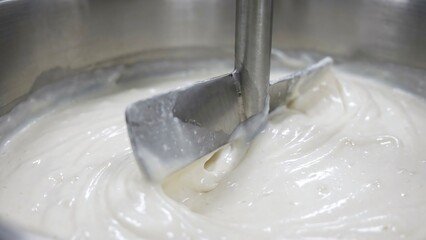 Industrial mixer blending a thick white substance within a metal container