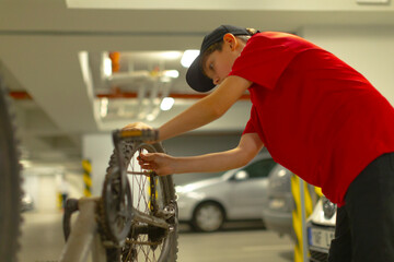 Teenager in bright clothing checks bike components before shift begins, Youthful courier in red top prepares bicycle wheels amidst busy city environment for upcoming delivery duties