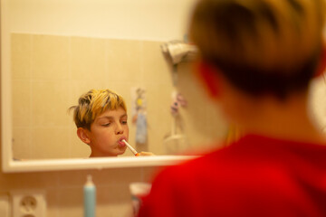 white boy brushing teeth in bathroom mirror with red shirt reflection, toothpaste foam and toothbrush visible, candid morning hygiene routine capturing personal care and sleepy wakeup