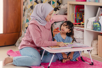 An Asian Muslim woman reading a fairy tale book to her daughter at home