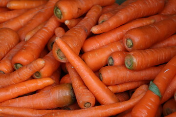 A pile of fresh carrots mixed with partially rotten ones stacked together, displaying varying shades of orange.