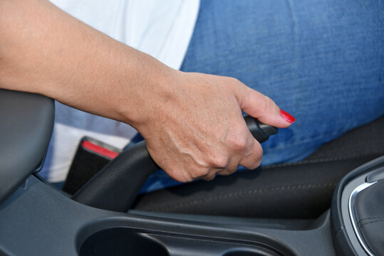 Hand female driver pulling the hand brake inside car