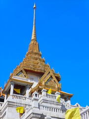 Fototapeta premium White marble and golden spires of Wat Traimit soar into a clear blue sky in Bangkok