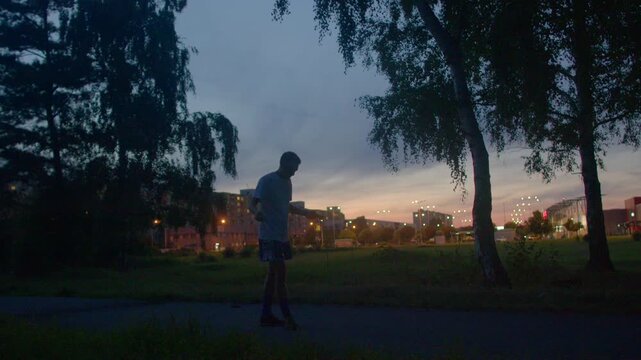 Gentle evening scene with contemplative male, Evening cityscape with man resting during sunset in park, Man standing calmly in city park during sunset with reflective mood and relaxed stance