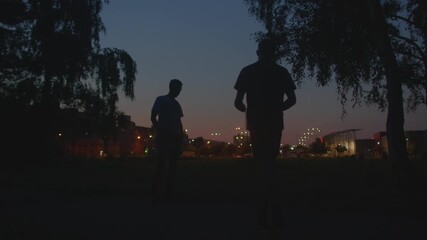 Urban silhouettes exercise as city lights shine, Men warm up with city skyline glowing in evening light, Social evening exercise with friends under glowing city skyline and urban surroundings