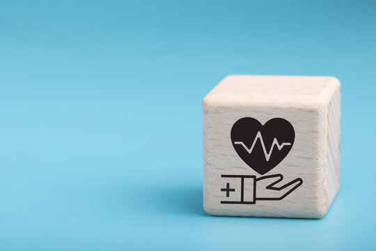 Health insurance concept. Healthcare, finance and medical service. Wooden cube block with hand holds heart pulse, heartbeat lone and cardiogram symbol. Healthcare, medical background and copy space.