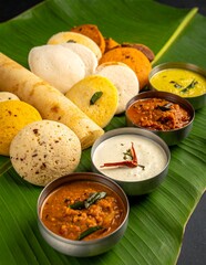 Traditional South Indian Breakfast Platter with Idli Dosa Vada and Chutneys Served on Banana Leaf.
