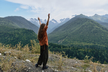 Person on a rocky overlook raises arms toward the expansive mountains landscape and valley, portraying freedom, adventure, and outdoor exploration in a pristine alpine scene