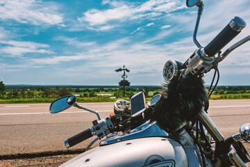 Motorcycle adventure on an open road under a vast blue sky, featuring a chrome cruiser, handlebars, and a dragon monument in the distance. Perfect for travel and freedom themes. © dizfoto1973