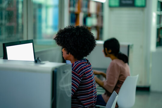 Students using desktop computers inside library study area showing digital research learning routine academic focus quiet education environment.
