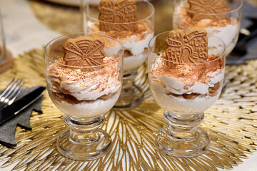 A delicious Christmas dessert, orange-flavored cream in glasses, sprinkled with cocoa powder and speculoos biscuit on top on a festively set table
