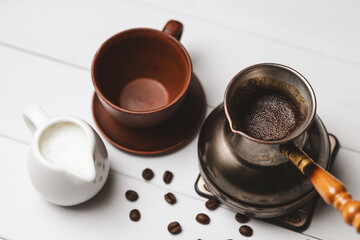 Turkish coffee in cezve with empty ceramic cup, milk pitcher and coffee beans on white rustic table