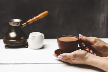 Cozy moment with female hands holding ceramic coffee cup, Turkish cezve, and milk pitcher on rustic white table