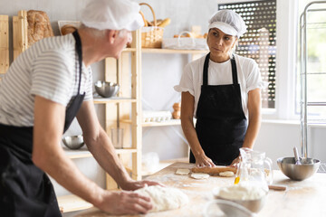 Two bakers prepare dough for baking - shaping it and rolling it out with rolling pin