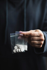 Close-up of female hand holding two transparent plastic bags with white narcotic powder and white pills, concept of drug abuse and drug trafficking