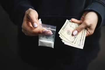 Close-up of female hands holding cash and transparent plastic bag with white narcotic powder, concept of drug abuse and drug trafficking