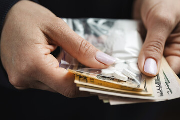 Close-up of hands holding cash and two transparent plastic bags with white powder and narcotic pills, concept of drug abuse and drug trafficking