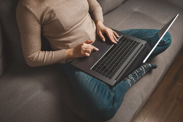 Woman sitting cross-legged on couch using laptop at home, concept of freelance work, remote job, online learning and e-commerce