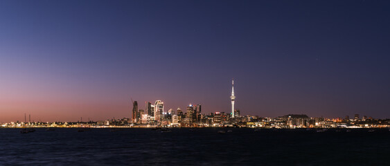 Panoramic view of Auckland city lights and Sky Tower at night across the harbor