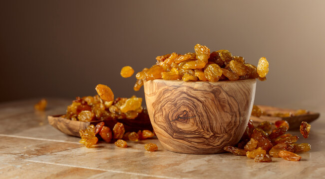 Yellow sultana raisins pour into a wooden bowl.