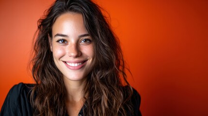 A joyful woman with curly hair smiles warmly, radiating positivity and approachability against a lively orange background, capturing the essence of happiness and connection.