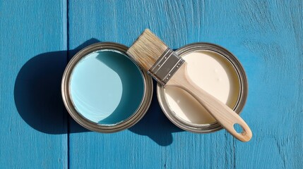 Two containers of paint, one cyan and one white, sit on a blue wooden surface with a clean paintbrush between them,