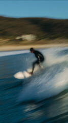 Surfer in black wetsuit powerfully carving a wave with background landscape motion blur