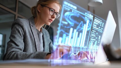 Focused female financial analyst wearing glasses studies digital stock market graphs and data displayed on her laptop in modern office environment - Powered by Adobe