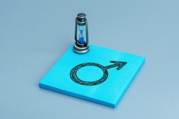 Male gender symbol hand drawn on a blue sticky note with a small hourglass. Male aging and life stages for men concept.